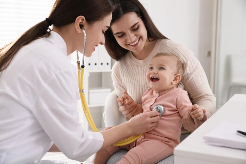 pediatrician listening to the heart of a smiling baby in her mother's arms